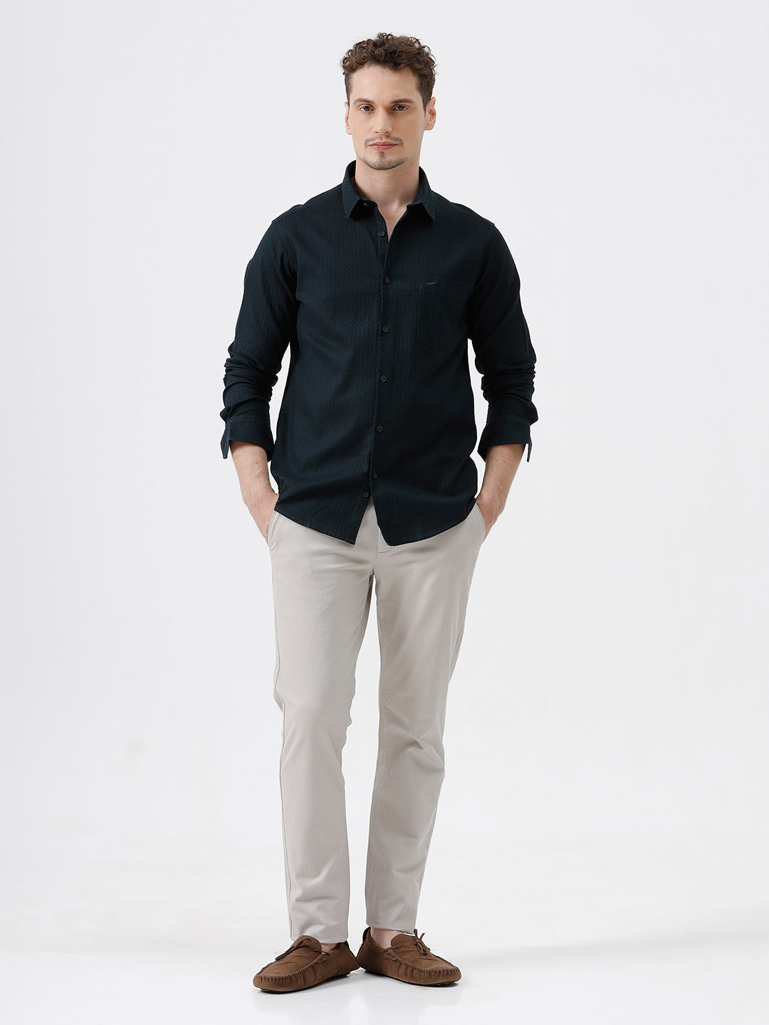 A man wearing a dark navy long-sleeve button-up shirt with a subtle textured pattern and light beige trousers, standing against a plain light gray background.