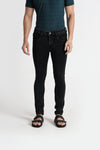 Man wearing a black black stone washed smoky black denim stretch fabric crocodile slim fit jeans on a light gray background
