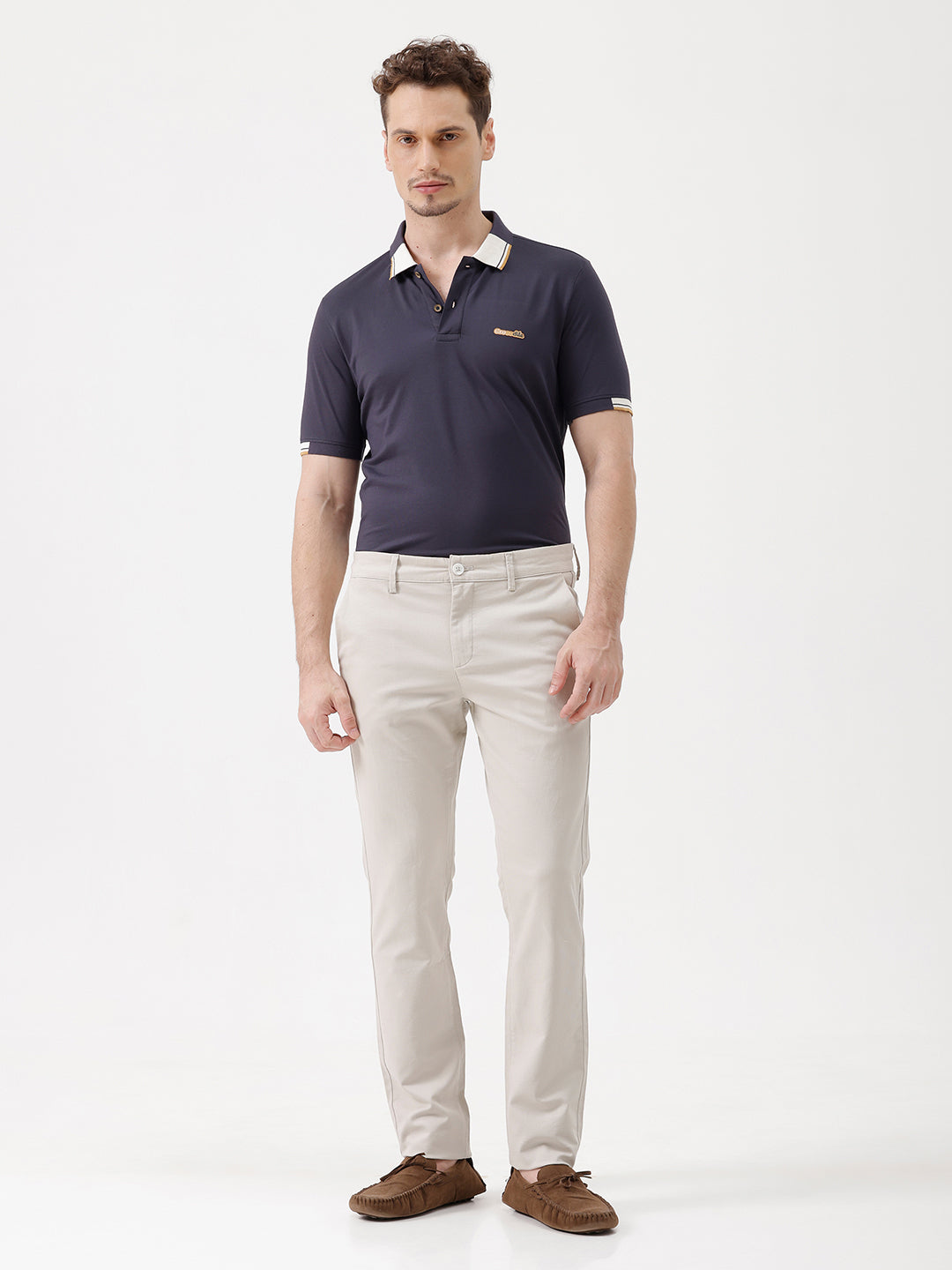 A man wearing a navy blue short-sleeve polo shirt with a contrasting cream and gold striped collar, paired with beige trousers, against a plain white studio background.