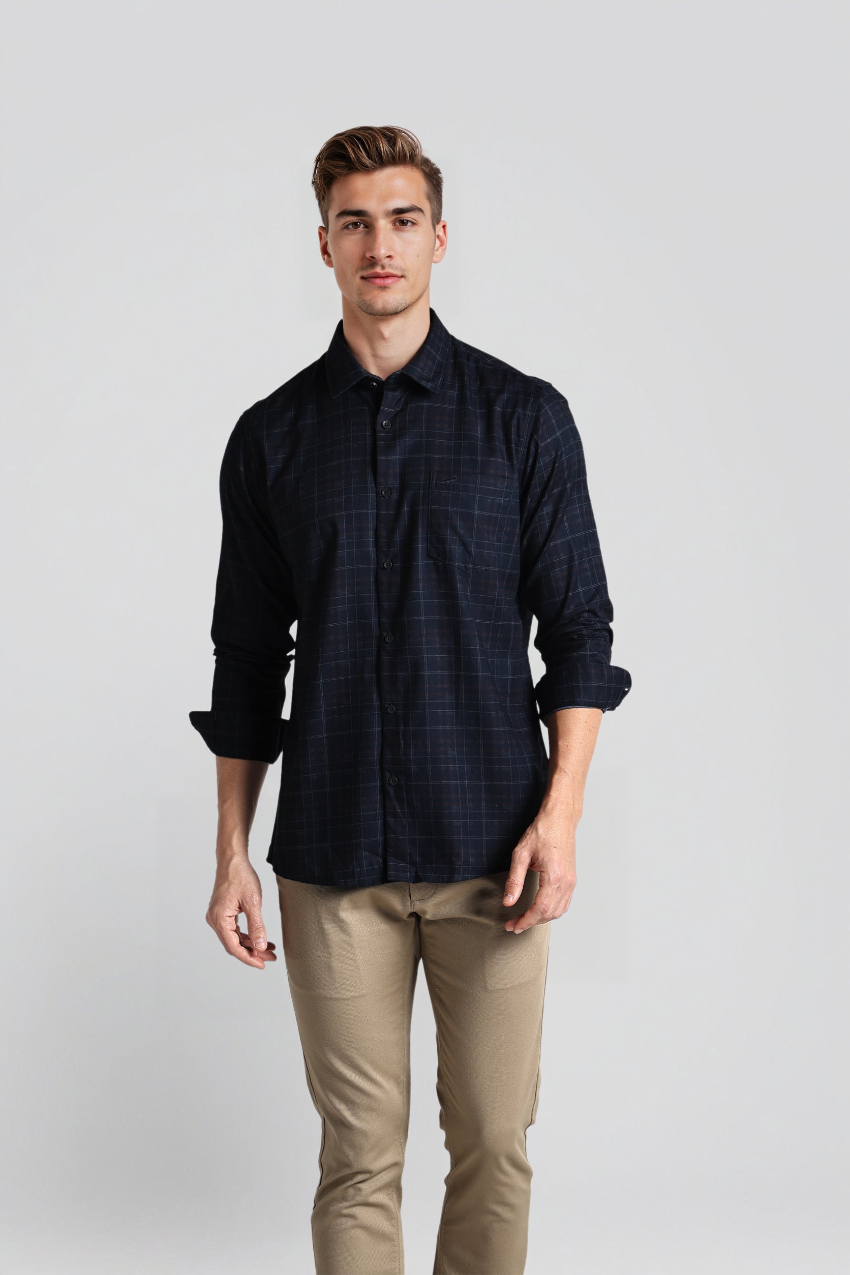 Man wearing a dark plaid shirt and beige pants against a plain background