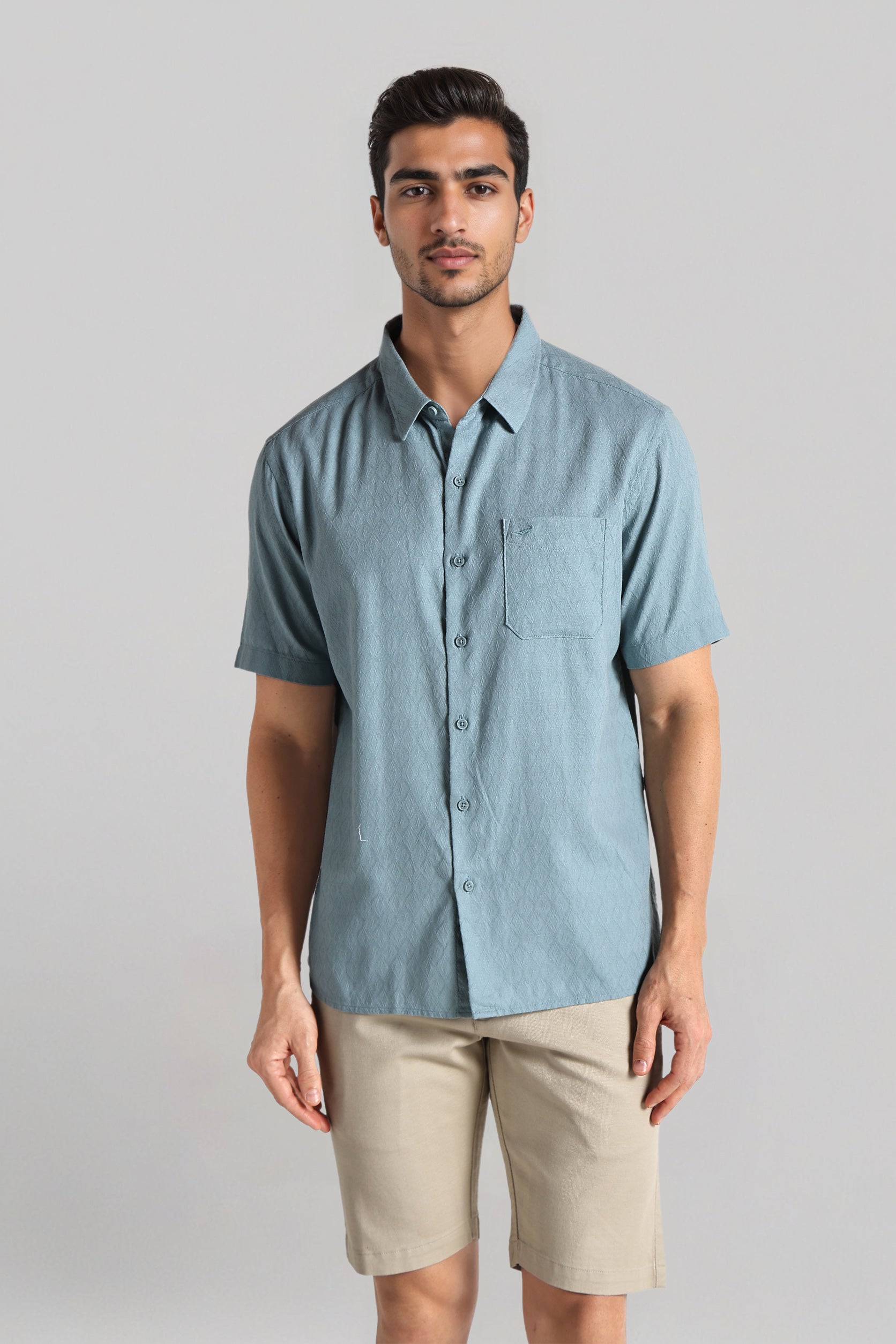 Man wearing a light blue button-up shirt and beige shorts on a gray background