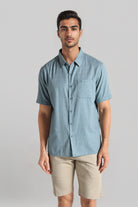 Man wearing a light blue button-up shirt and beige shorts on a gray background