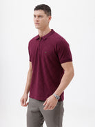 A man wearing a short-sleeve polo shirt in deep burgundy with a subtle textured geometric pattern, styled with gray trousers, sunglasses, and a watch against a plain white background.
