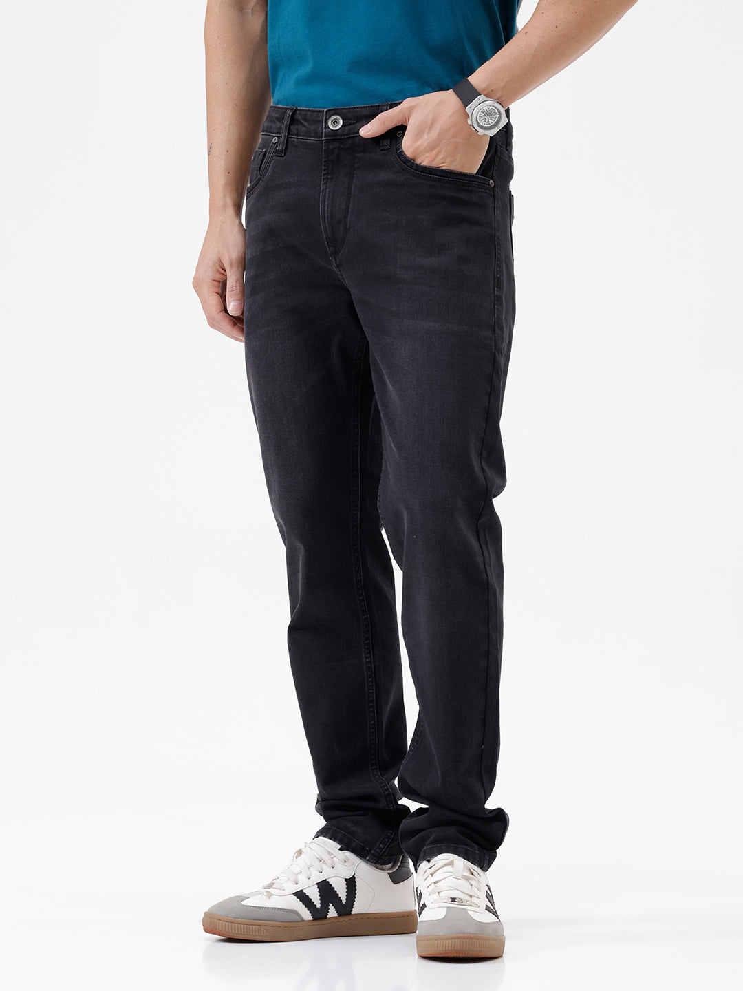 A person wearing slim-fit black jeans, a teal t-shirt, and white sneakers with gray accents, standing against a clean white studio background.