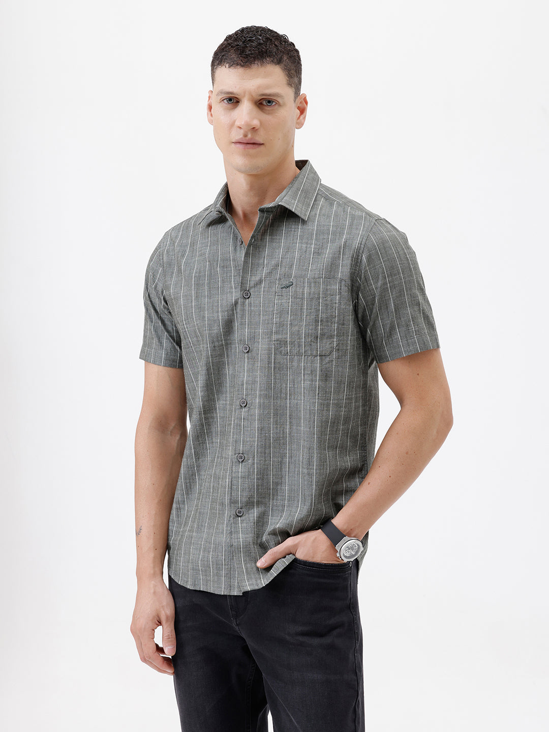 A man wearing a short-sleeve button-up shirt with a gray and white vertical stripe pattern, paired with black pants, standing against a plain white studio background.