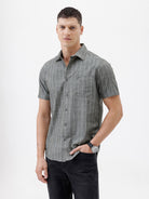 A man wearing a short-sleeve button-up shirt with a gray and white vertical stripe pattern, paired with black pants, standing against a plain white studio background.