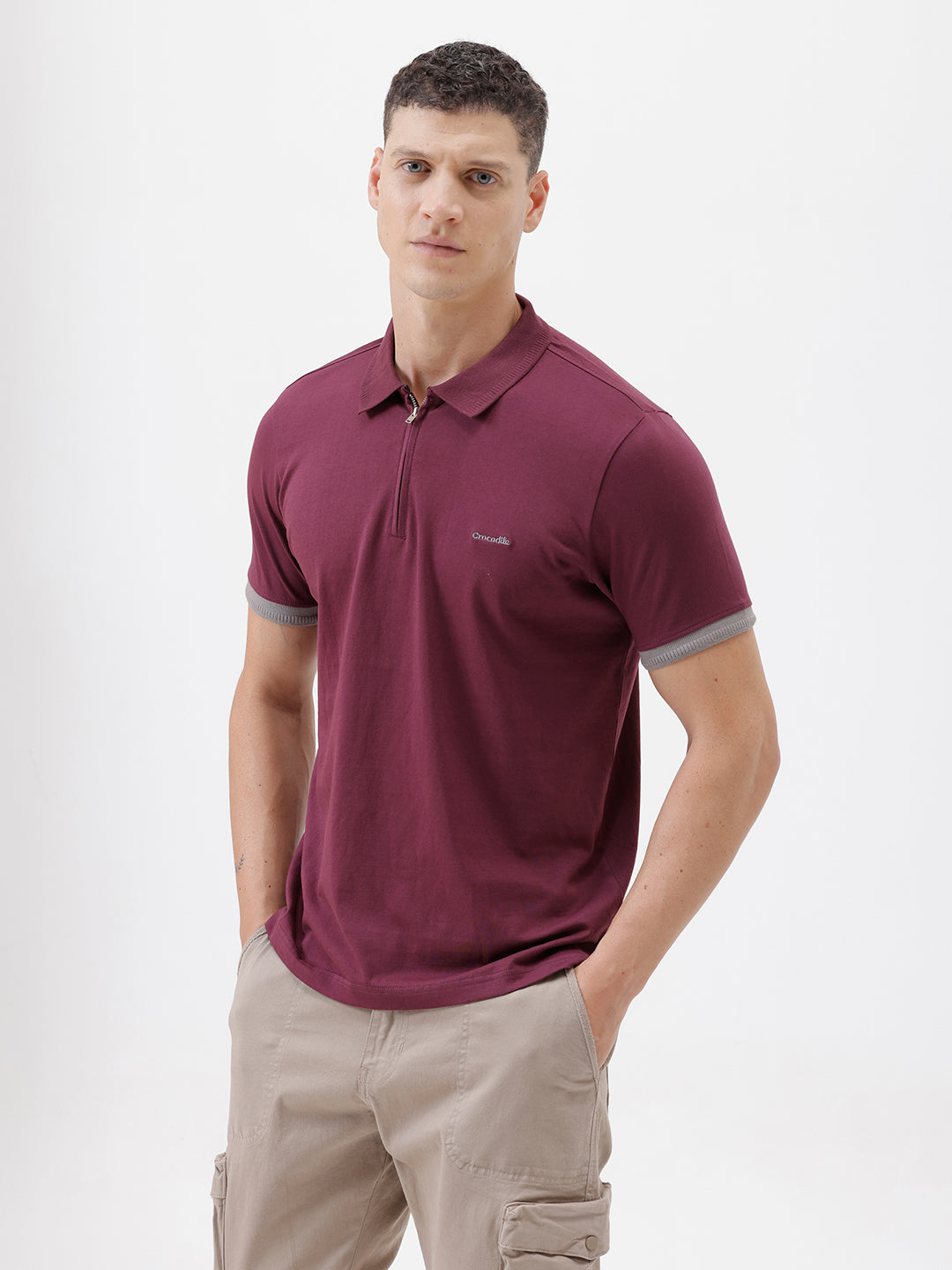 A man wearing a short-sleeve polo shirt in maroon with gray sleeve trim and a half-zip collar, paired with beige cargo pants, against a plain white studio background.