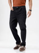 A person wearing black slim-fit jeans, paired with a rust-orange t-shirt and brown sneakers, shown from the waist down against a plain white studio background.