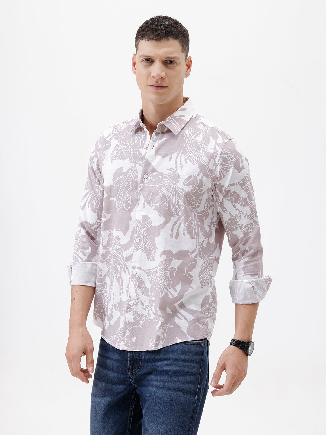 A man wearing a long-sleeve button-up shirt with a light gray and white abstract floral pattern, paired with dark blue jeans, standing against a plain white background.