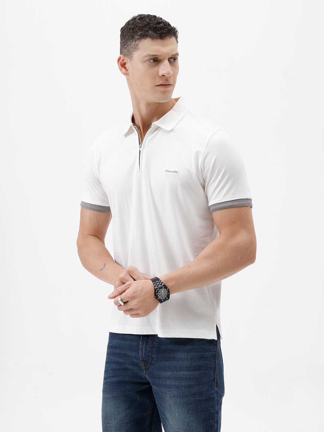 A man wearing a white short-sleeve polo shirt with gray ribbed trim on the collar and sleeve cuffs, paired with dark blue jeans, photographed against a plain white studio background.