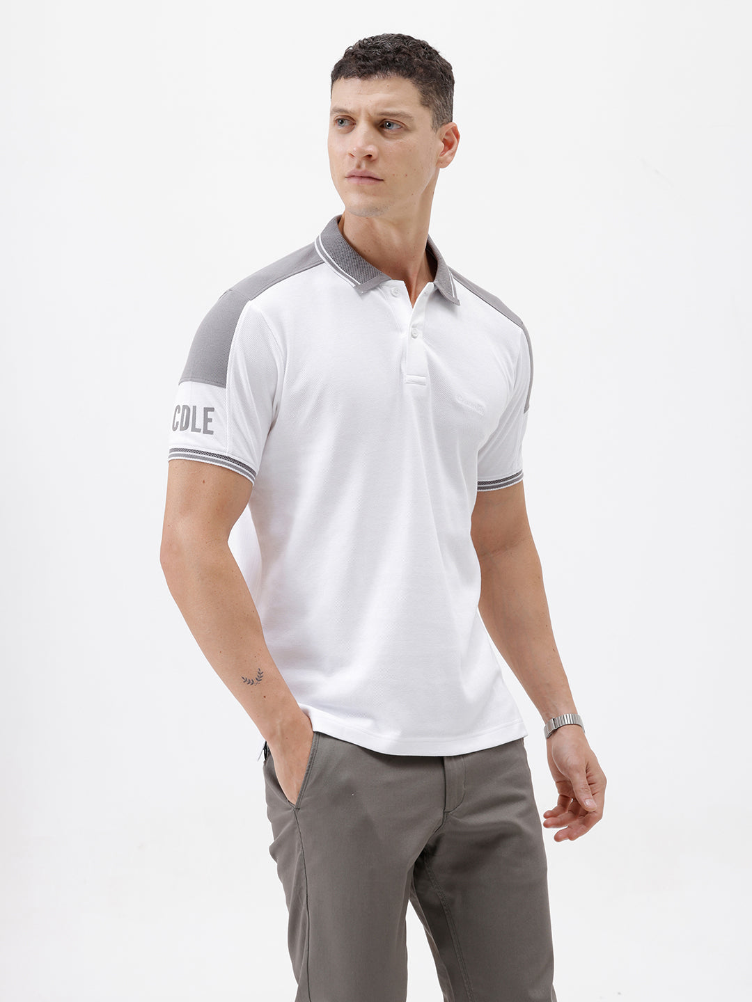 A man modeling a white short-sleeve polo shirt with gray shoulder panels and gray striped trim on the sleeves, paired with gray trousers and black sunglasses, against a plain white background.