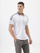 A man modeling a white short-sleeve polo shirt with gray shoulder panels and gray striped trim on the sleeves, paired with gray trousers and black sunglasses, against a plain white background.