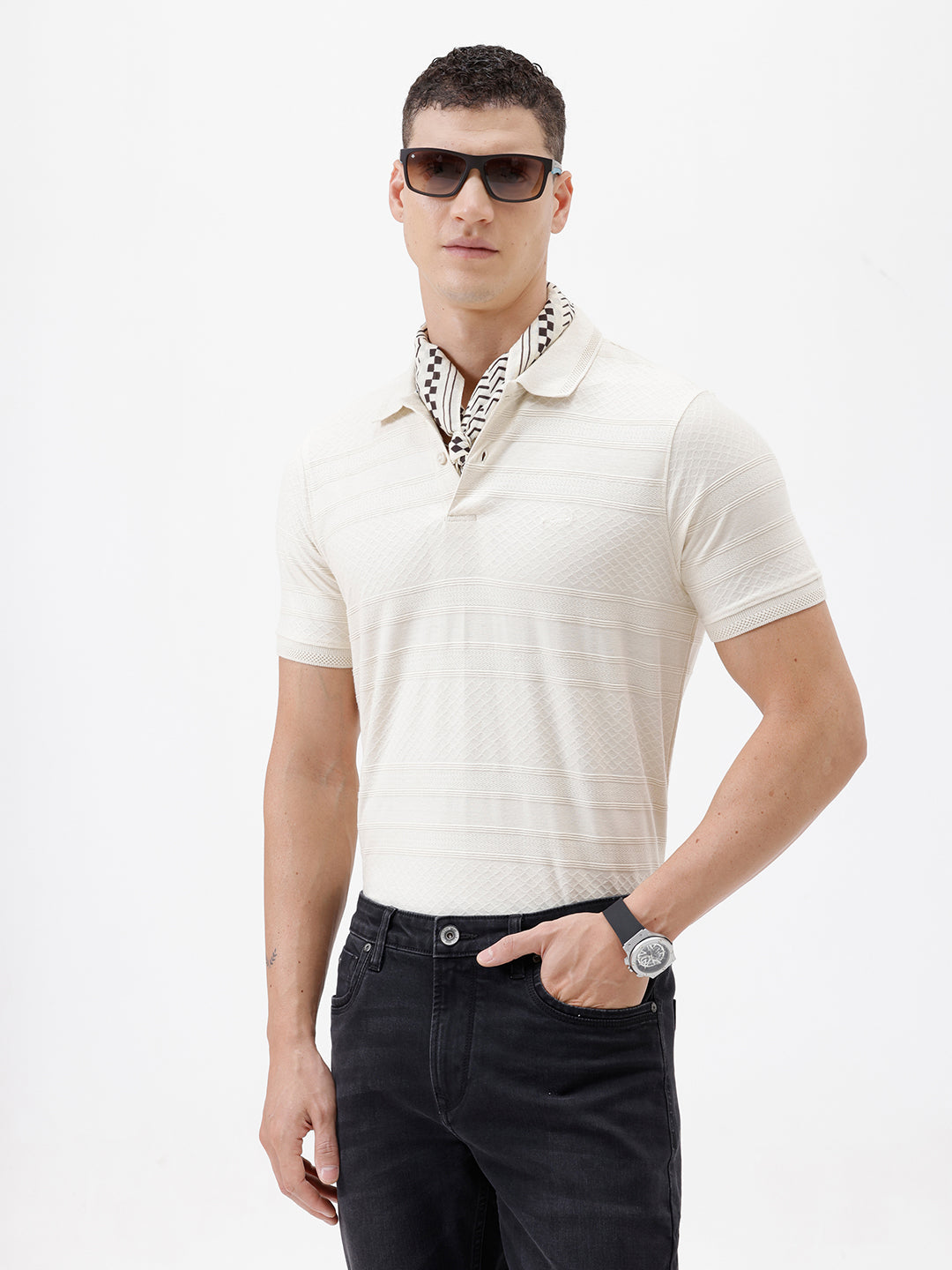 A man wearing a short-sleeve polo shirt in cream with subtle horizontal textured stripes, paired with dark jeans, standing against a plain white studio background.