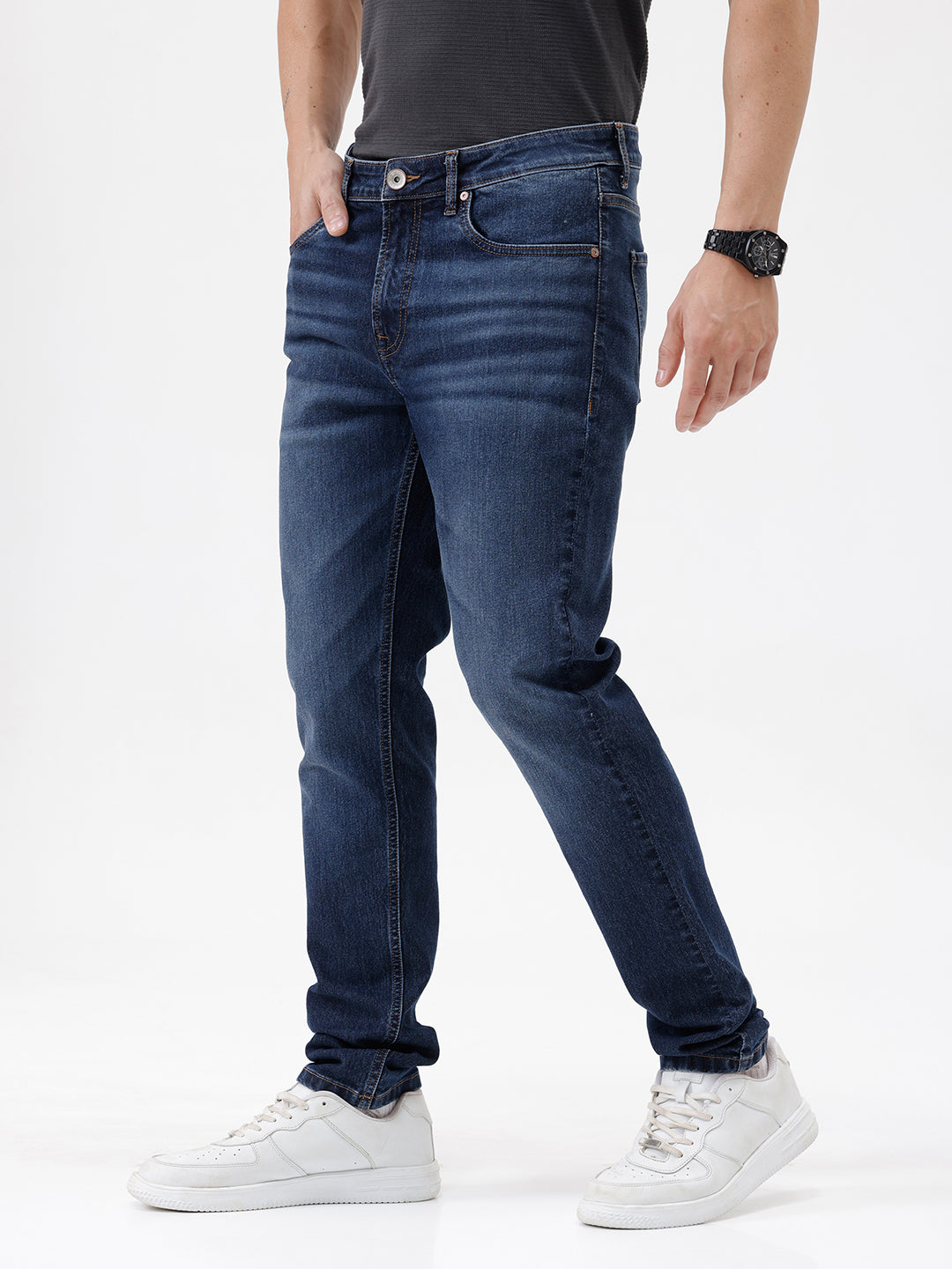 A person wearing dark blue slim-fit jeans with a faded wash, paired with a black t-shirt and white sneakers, shown from the waist down against a plain white studio background.