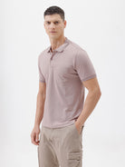 A man modeling a short-sleeve polo shirt in a dusty mauve-pink color, paired with khaki cargo pants and a baseball cap, against a plain light gray background.