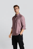 Man wearing a mauve button-up shirt and black pants on a light gray background