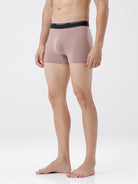 Person wearing a pair of beige boxer briefs with a black waistband on a white background