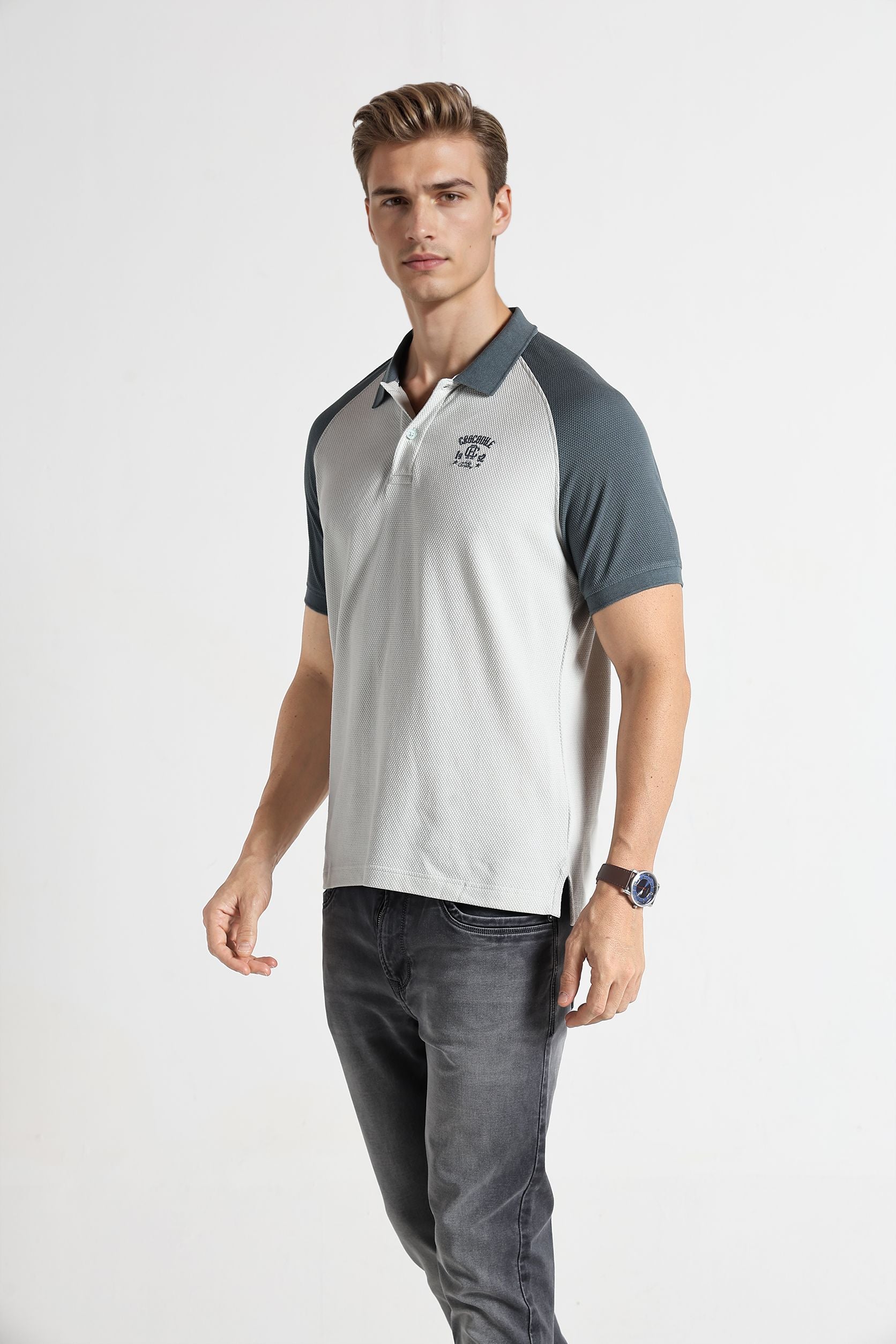 Man wearing a gray and white polo shirt with dark jeans on a white background