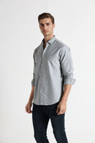 Man wearing a light gray button-up shirt and dark pants on a white background