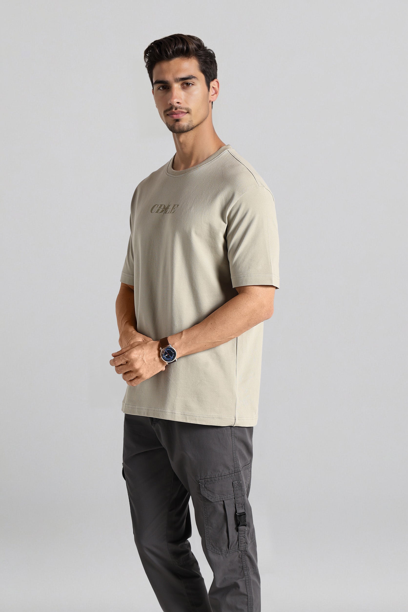 Man wearing a beige t-shirt and gray cargo pants on a light gray background