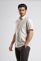 Man wearing a beige short-sleeve shirt and dark pants on a white background