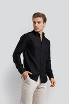 Man wearing a black shirt and light-colored pants against a white background