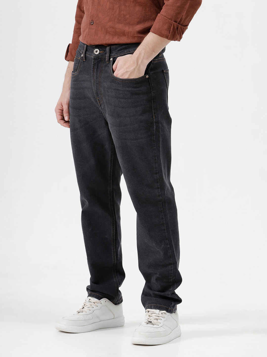 A person wearing dark charcoal gray slim-fit jeans, a rust-brown long-sleeve button-up shirt, and white sneakers, standing against a plain white studio background.