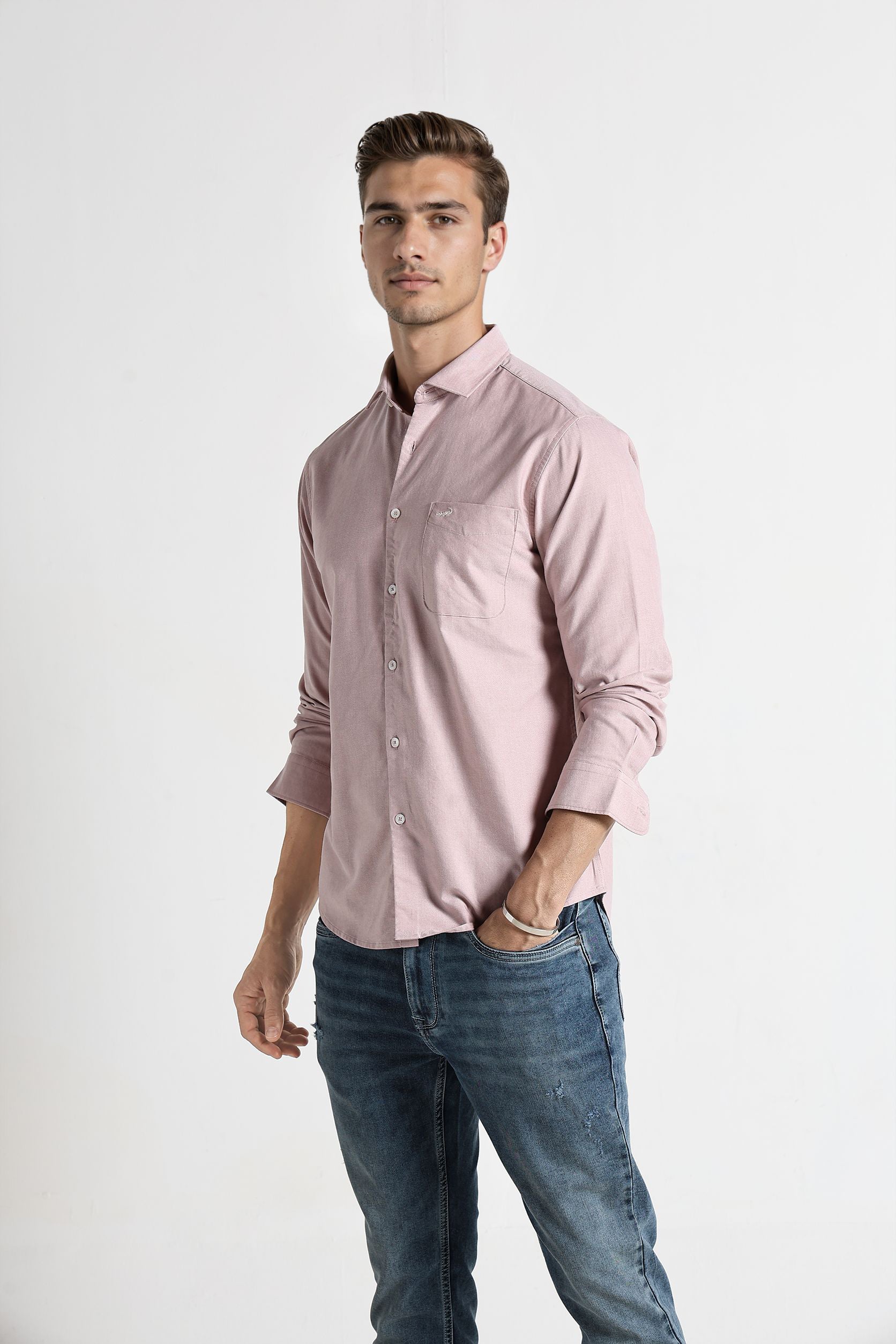Man wearing a light pink shirt and blue jeans on a white background