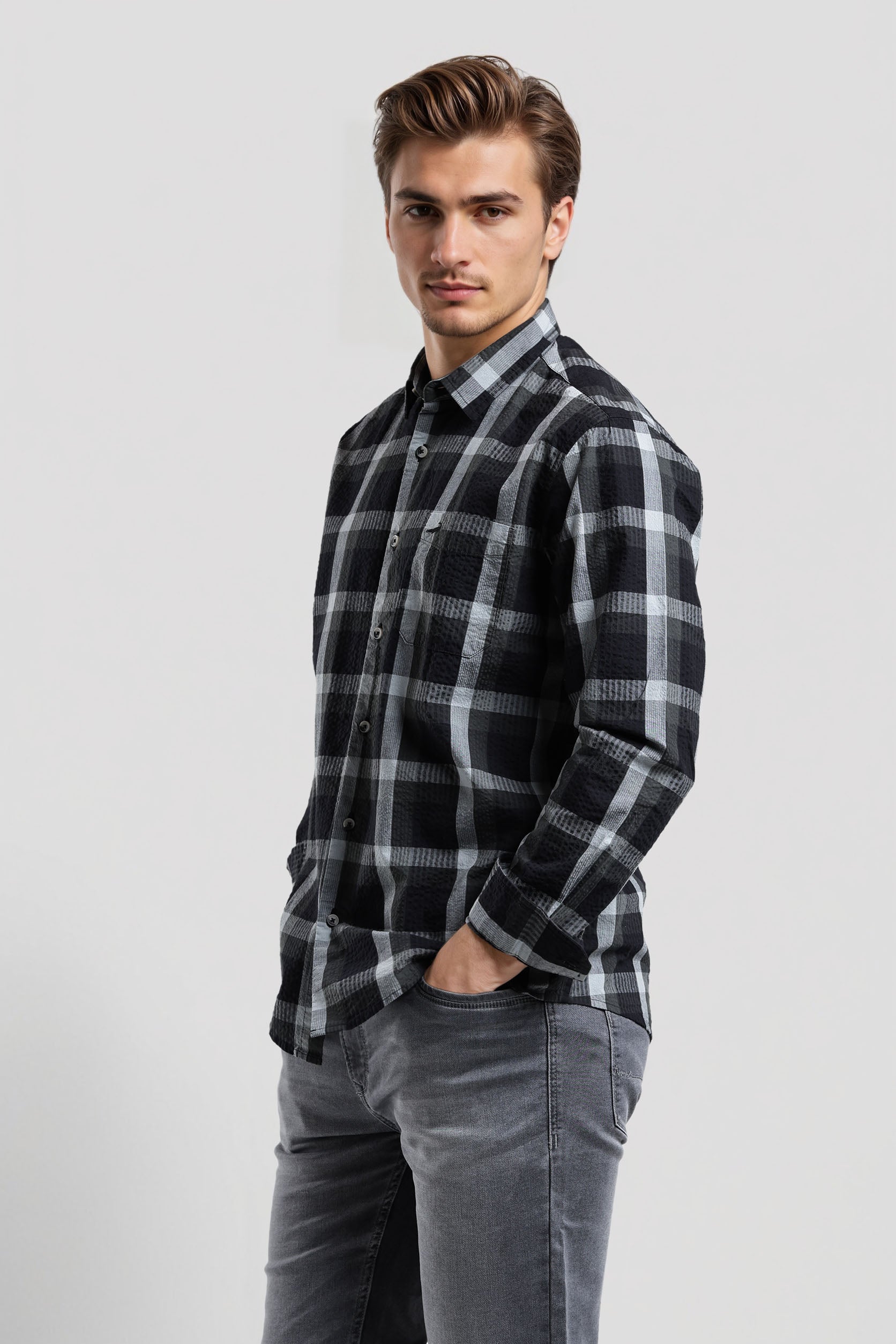 Man wearing a black and gray plaid shirt with gray jeans on a white background