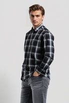 Man wearing a black and gray plaid shirt with gray jeans on a white background