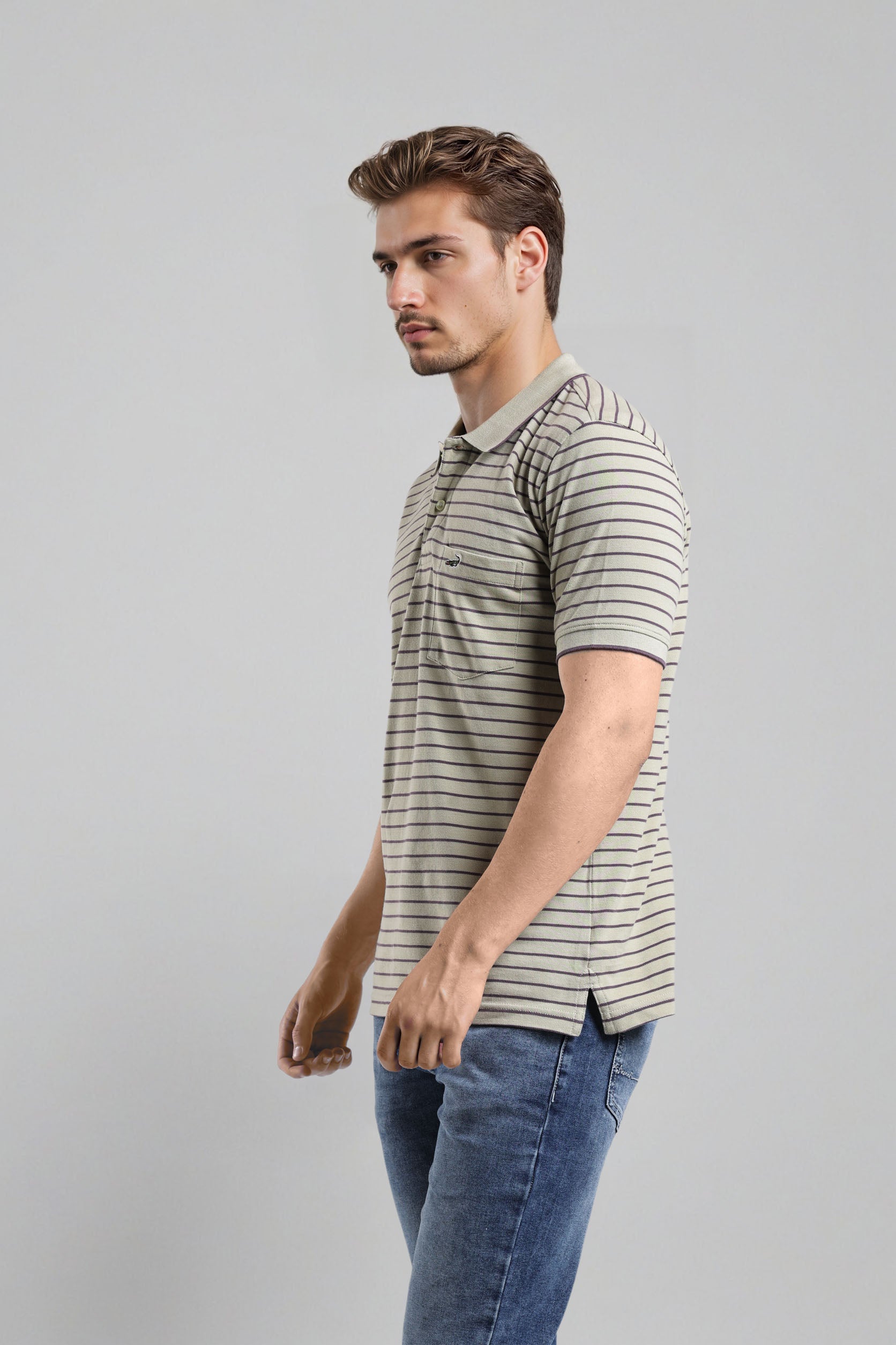 Man wearing a striped polo shirt and jeans on a gray background