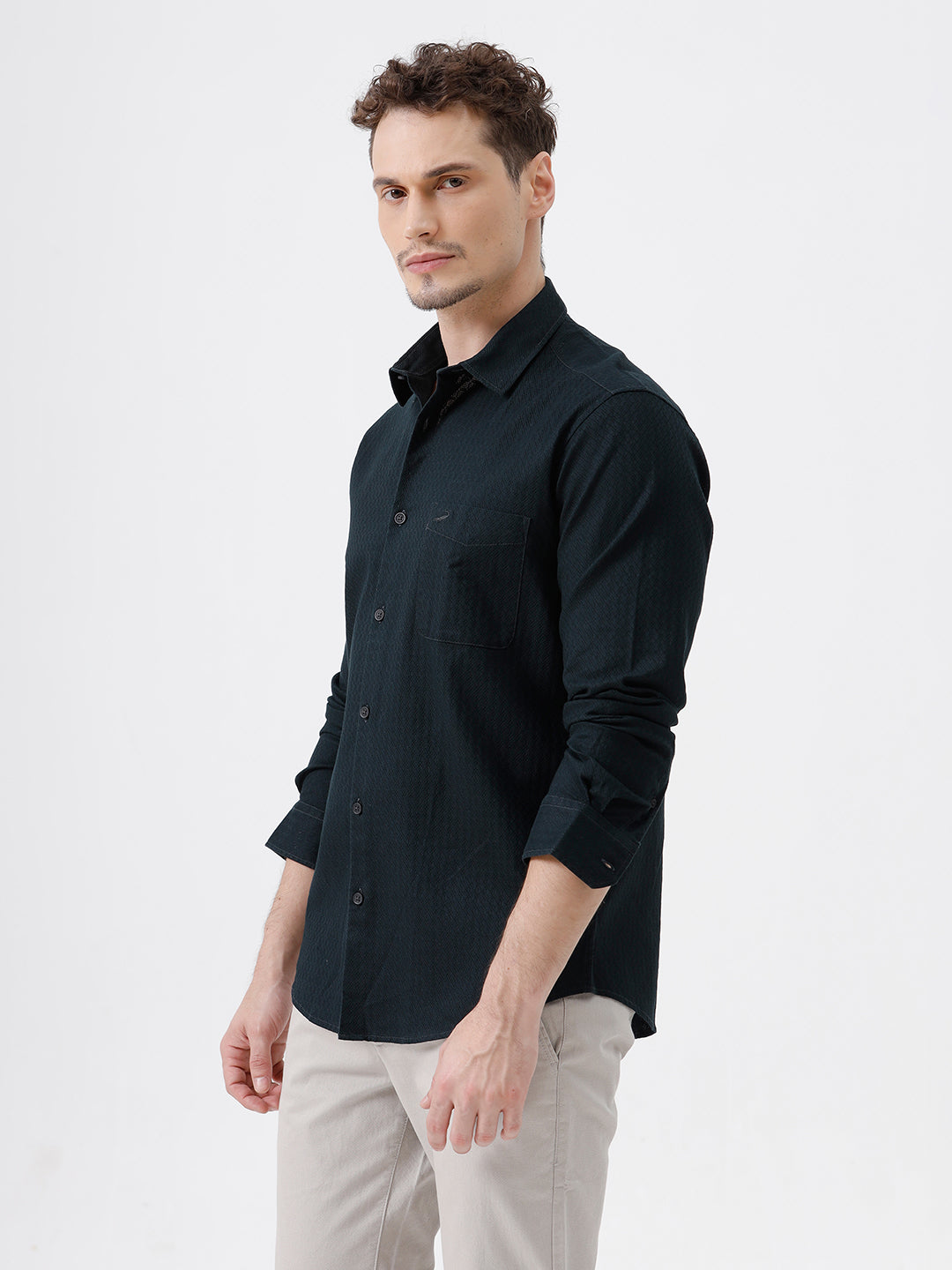 A man wearing a dark navy long-sleeve button-up shirt with a subtle textured pattern and light beige trousers, standing against a plain light gray background.