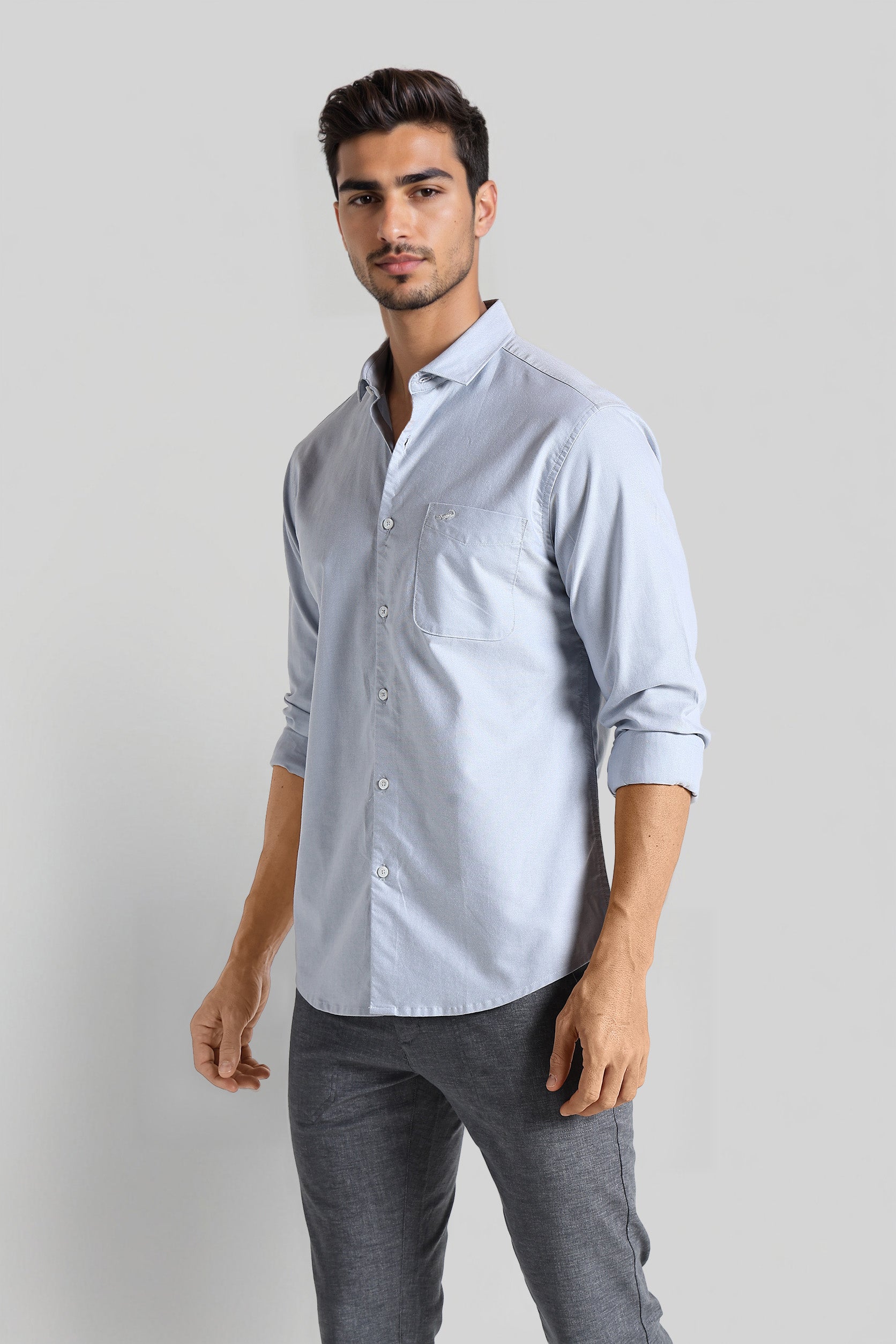 Man wearing a light blue button-up shirt and gray pants on a white background