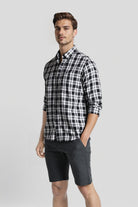 Man wearing a black and white checkered shirt and dark shorts on a light gray background