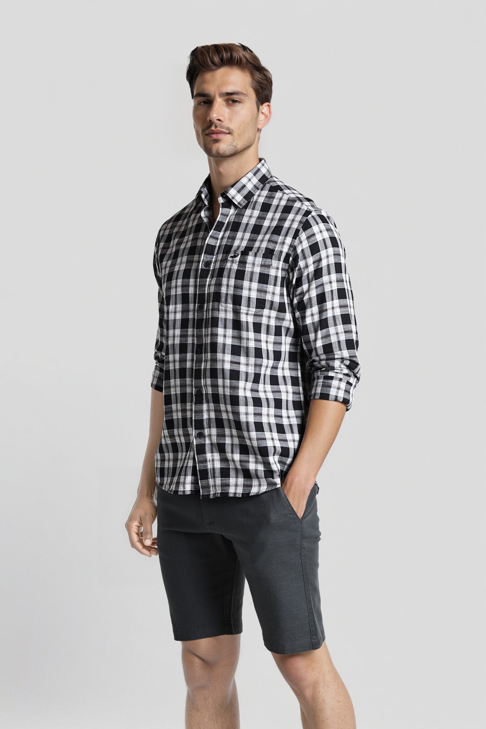 Man wearing a black and white checkered shirt and dark shorts on a light gray background