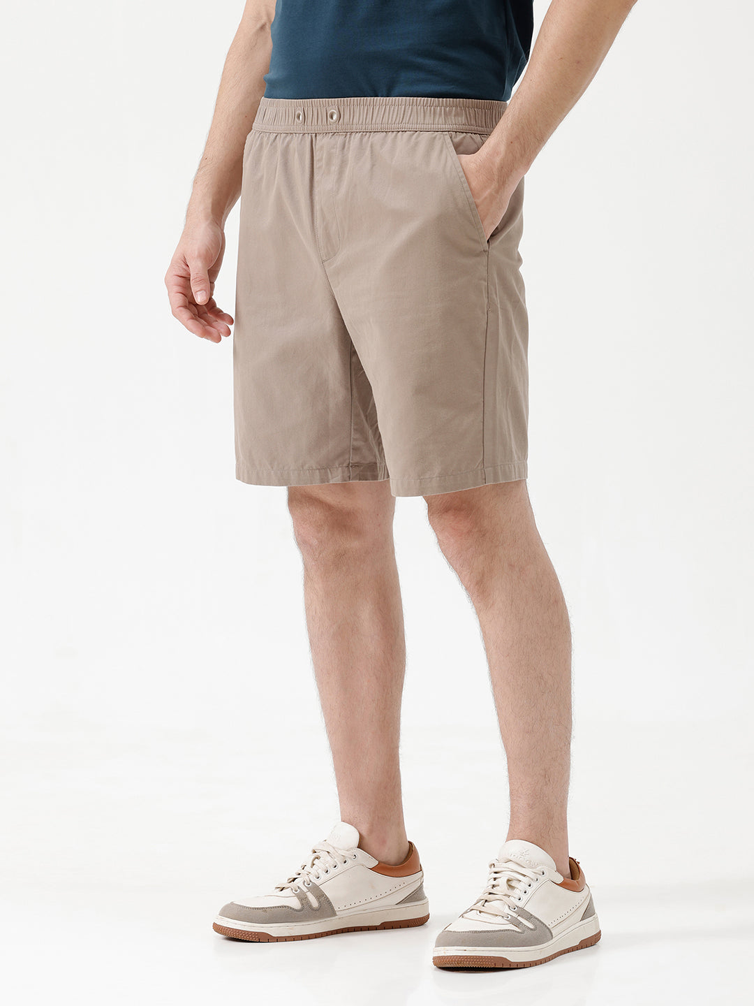 A person wearing beige drawstring shorts, a navy blue t-shirt, and white sneakers, shown from the waist down against a plain white studio background.