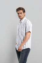 Man wearing a white striped shirt and dark jeans against a gray background