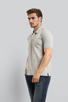 Man wearing a light gray polo shirt and dark jeans on a plain background