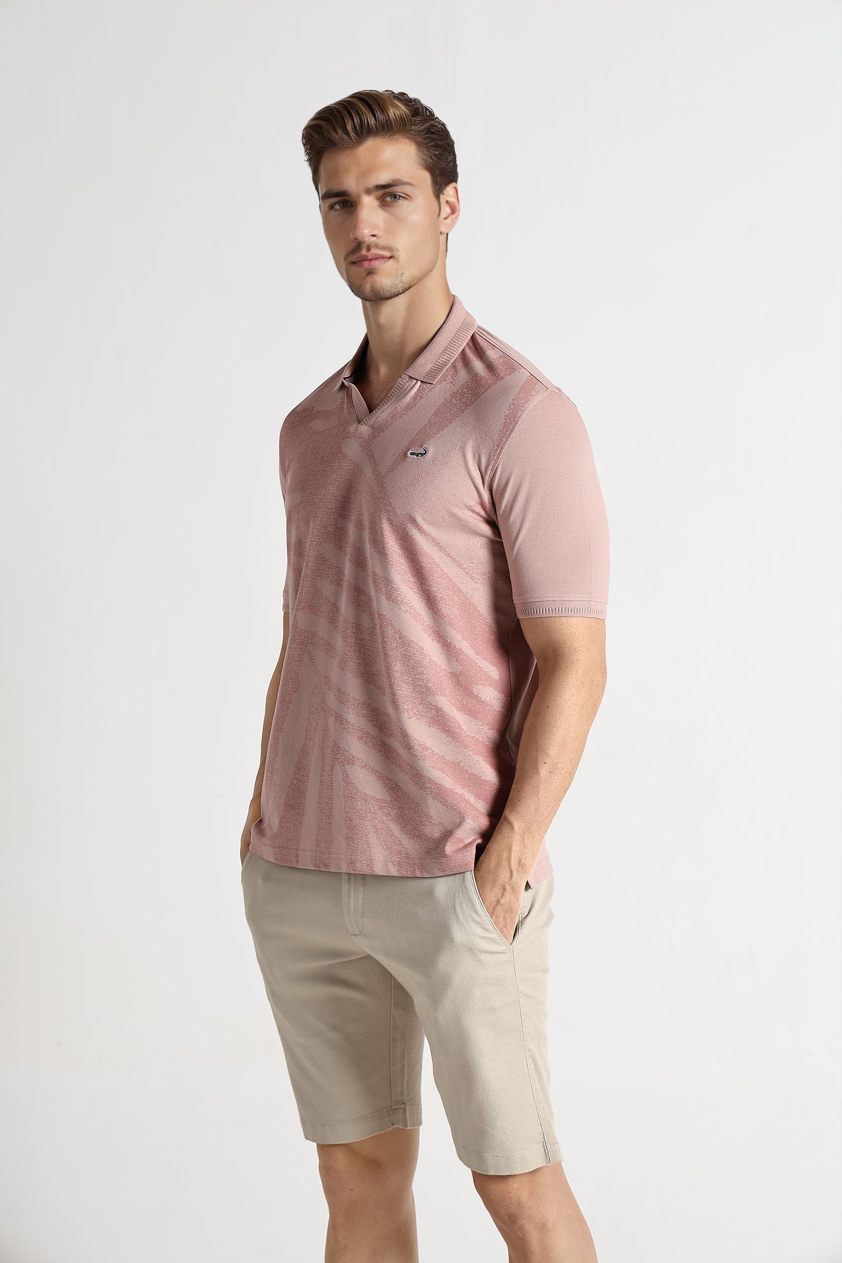 Man wearing a pink polo shirt and beige shorts on a white background