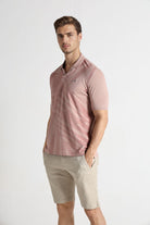 Man wearing a pink polo shirt and beige shorts on a white background