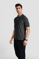 Man wearing a dark gray polo shirt and black pants on a light gray background