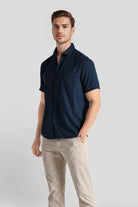 Man wearing a navy blue shirt and beige pants on a light gray background