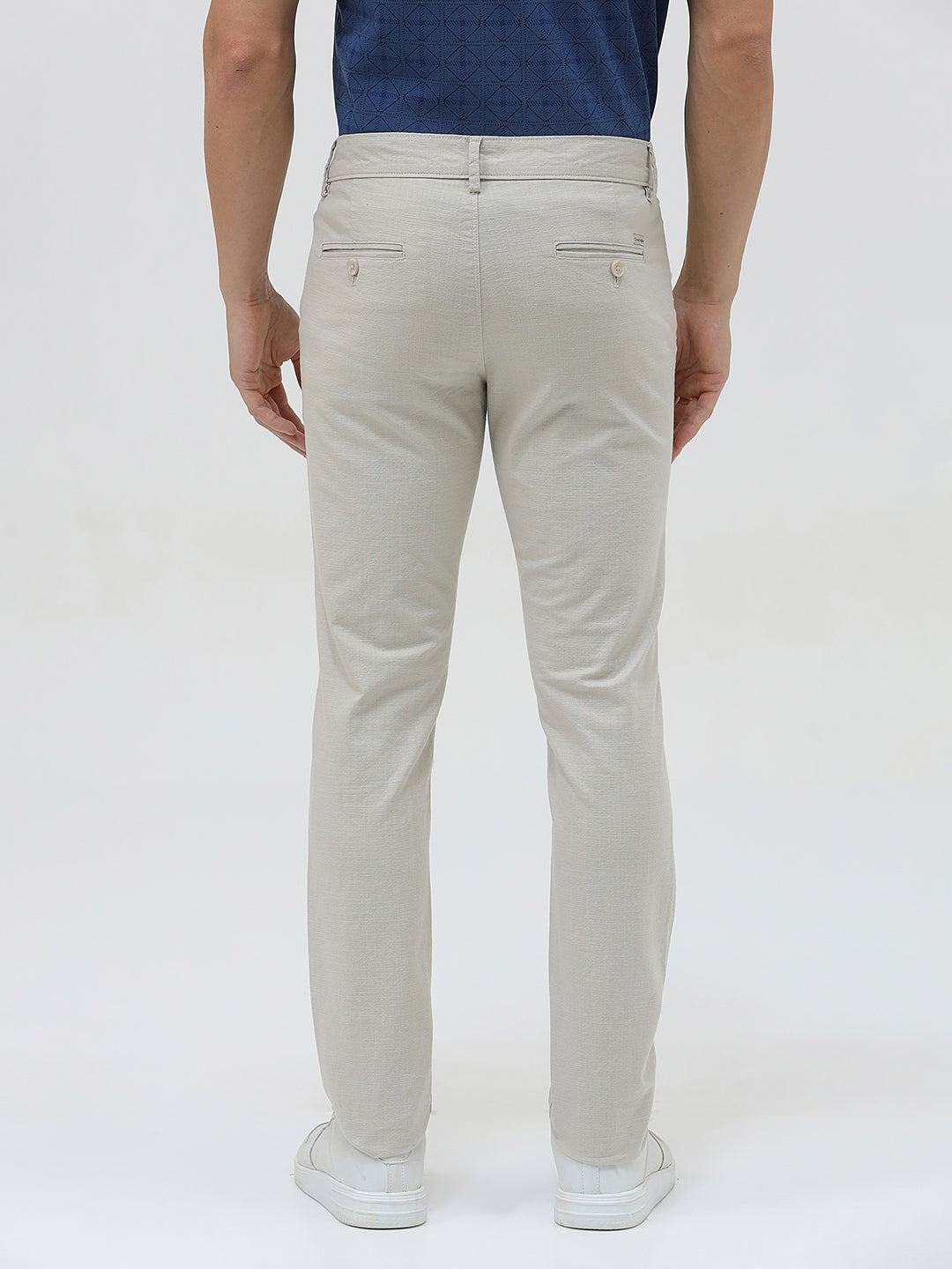 A person wearing light beige slim-fit chino pants, a navy blue t-shirt, and white sneakers, standing against a plain white studio background.
