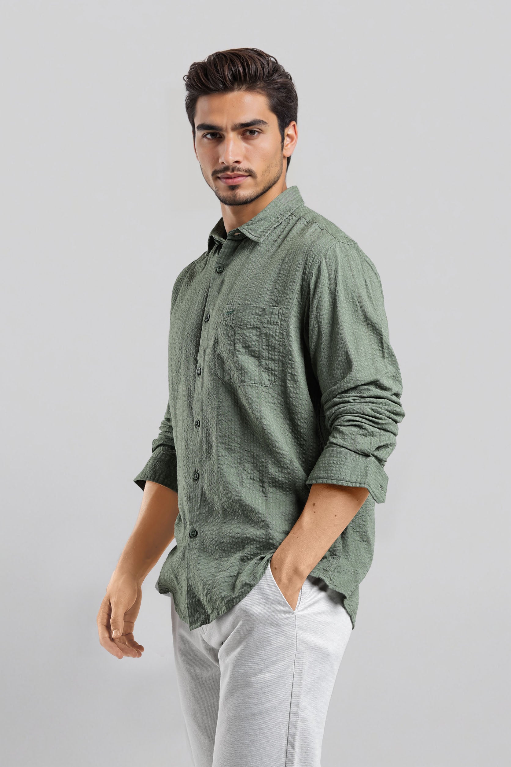 Man wearing a green checkered shirt and white pants on a gray background