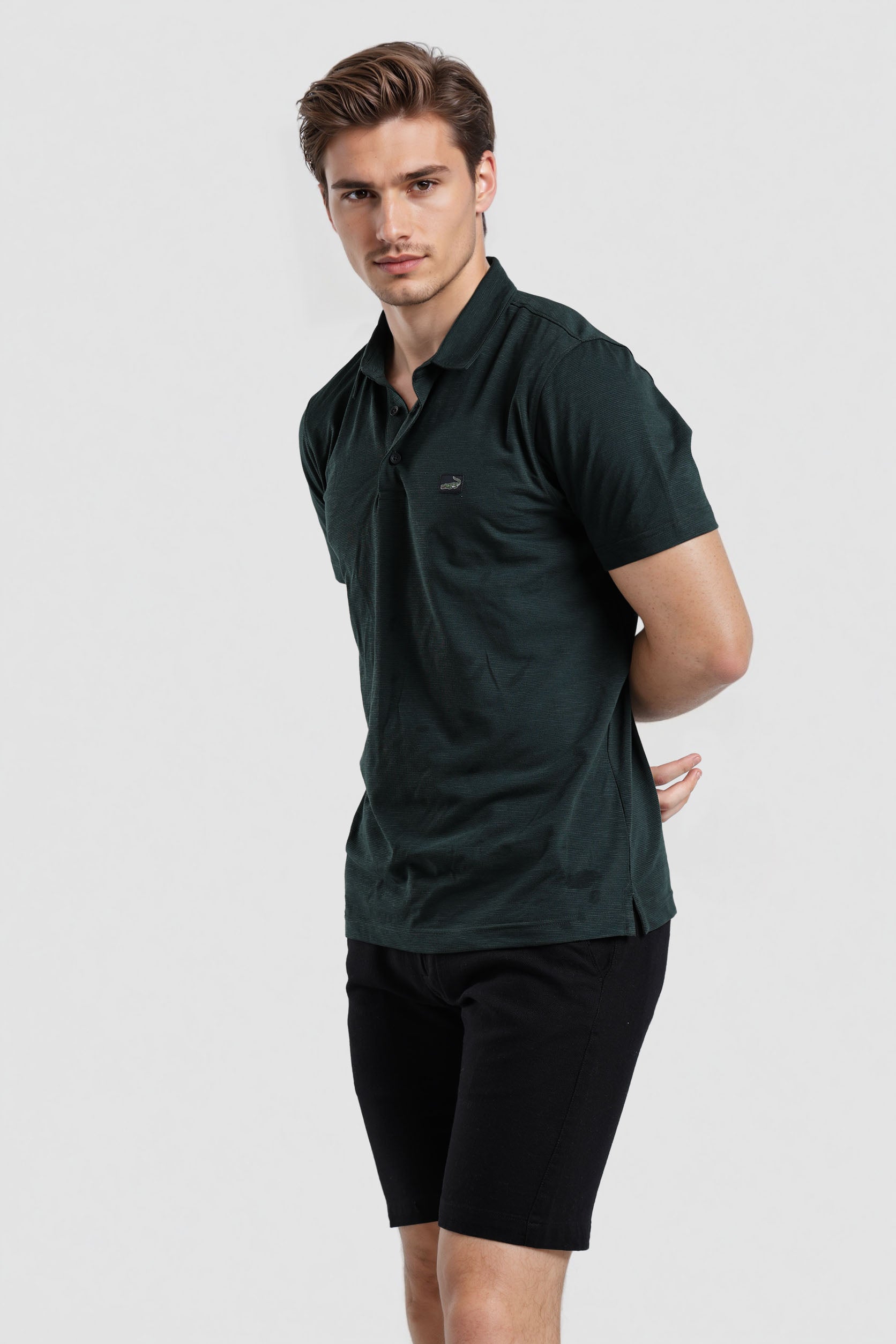 Man wearing a dark green polo shirt and black shorts on a light gray background