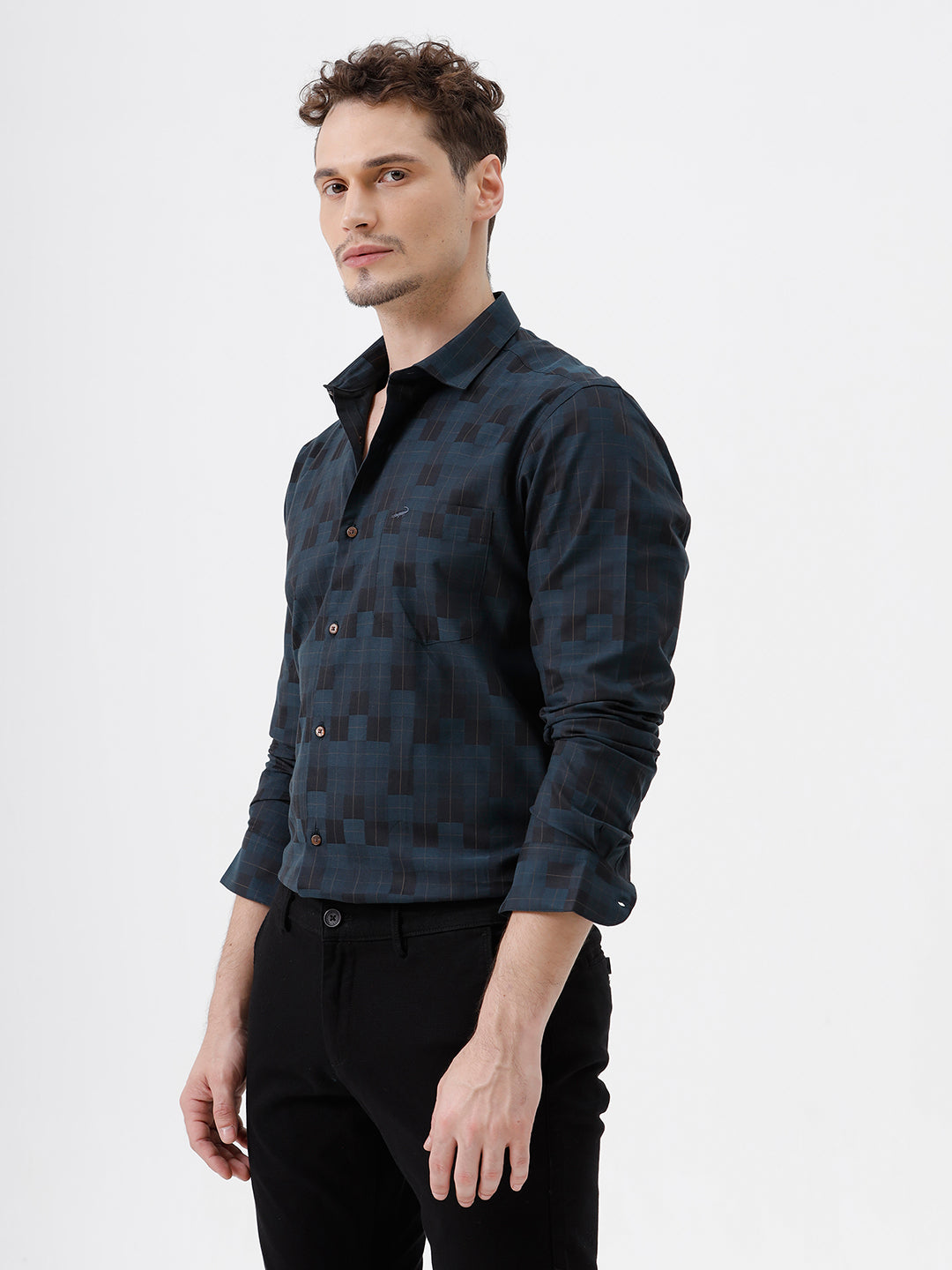 A man wearing a dark navy blue patterned long-sleeve button-up shirt and black trousers, standing against a plain white studio background.