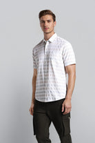 Man wearing a white patterned shirt and black pants on a gray background