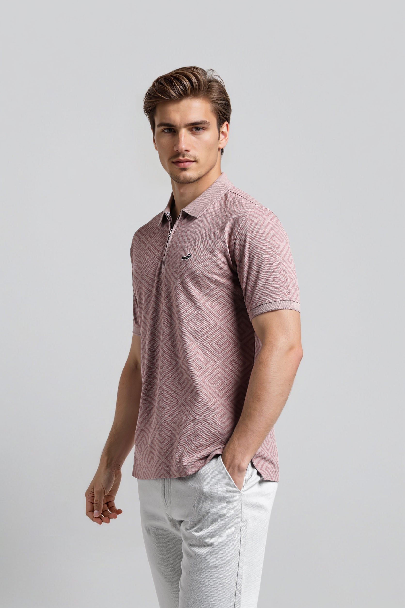 Man wearing a patterned pink shirt and light gray pants against a plain background