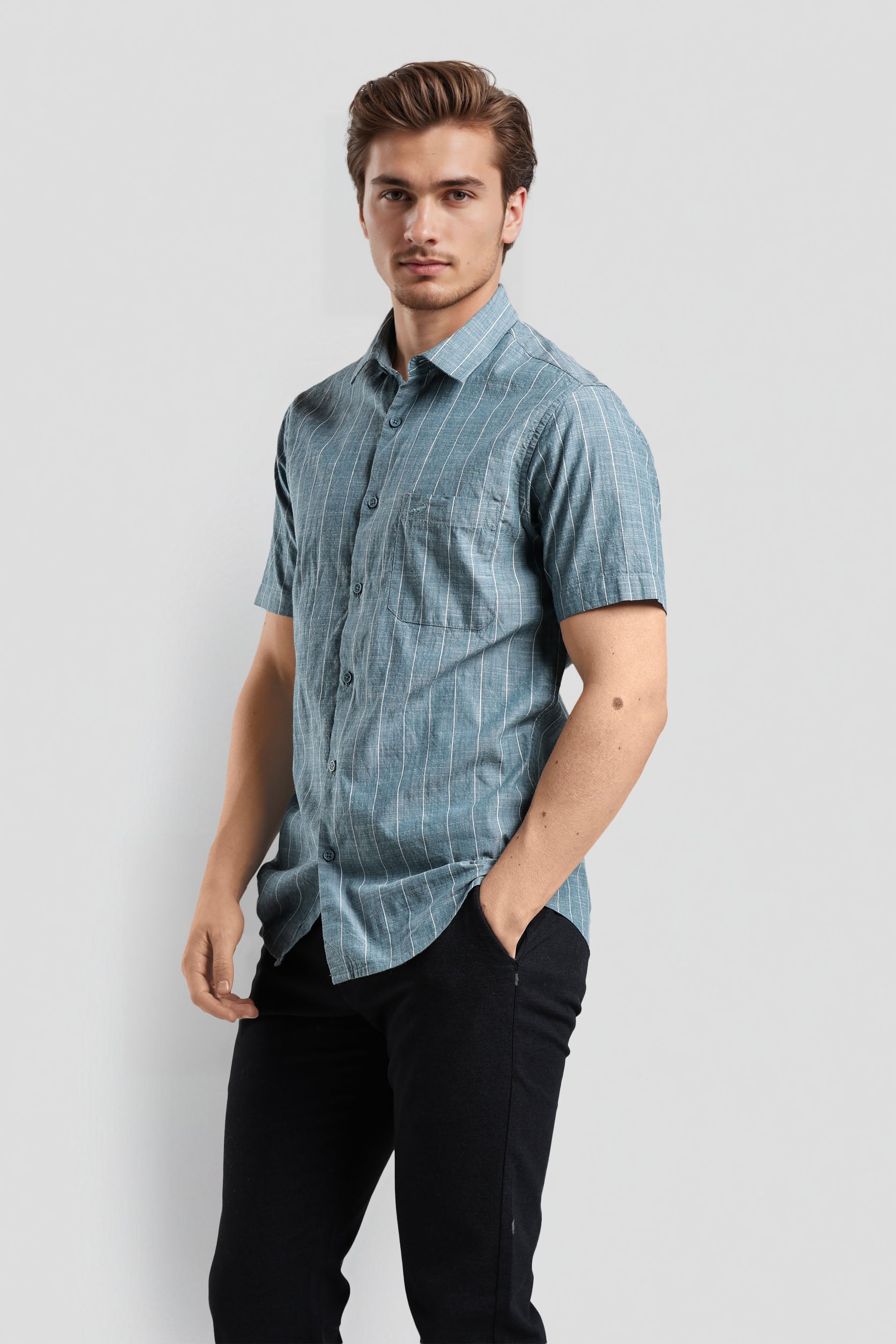 Man wearing a blue checkered shirt and black pants on a light gray background