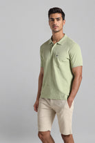 Man wearing a light green polo shirt and beige shorts on a gray background